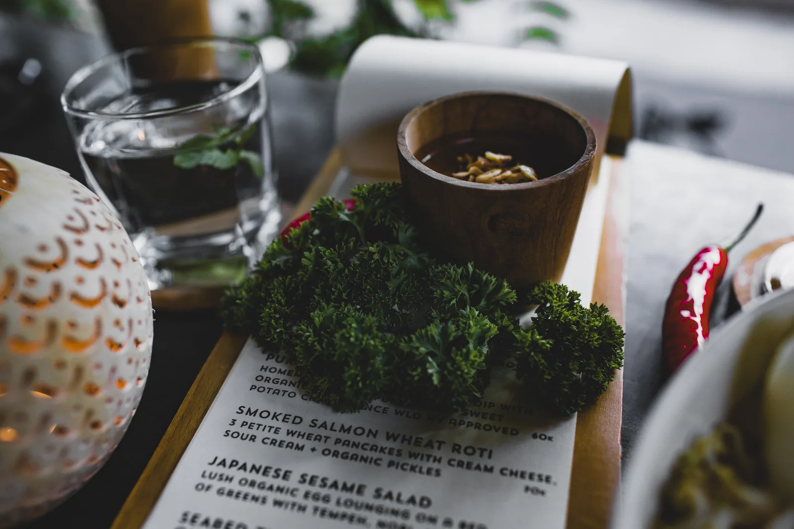 High angle table with bunch of fresh green curly parsley placed on menu with sauce cup near glass of water