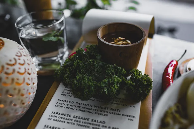 High angle table with bunch of fresh green curly parsley placed on menu with sauce cup near glass of water. Leverantörsavtal och inköp för restauranger: så bygger du en leveranskedja som håller
